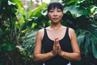 Yukarı selamlama pozunda yoga yapan Asyalı bir kızın portresi. Uyum ve akıl sağlığı. Spor kıyafetleri giyen ve Bali Adası 'ndaki bahçeye bakan genç ve ciddi bir kadının kırpılmış görüntüsü.