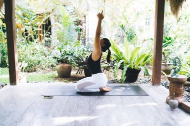 Tahta terasta yoga yapan Asyalı kızın yan görüntüsü. Uyum ve akıl sağlığı. Gözleri kapalı, spor giyimli ve spor minderinde çıplak ayaklı güzel bir kadın. Bali adası. Güneşli bir gün