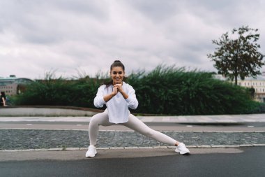 Genç ve mutlu kadın, şehirde sabah egzersizleri sırasında basit ve etkili egzersizler yaparak bacak ve kalça kaslarını pompalamak için derin hamleler yapıyor. Sağlıklı yaşam tarzı, vücudunu formda tutan bir kadın.