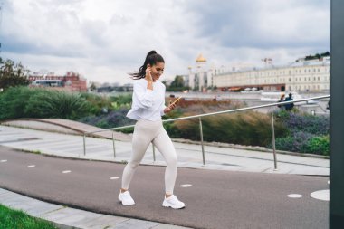 Genç esmer kadın şehir parkında yürüyor ve cep telefonu uygulamasına bağlı kablosuz kulaklıkla müzik dinlemekten zevk alıyor. Akıllı telefondan mesaj okuyan çekici bir kadın ve müzik listesinin keyfini çıkarın.