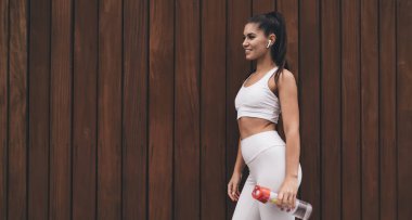 Reklam metni için arka planda duran kablosuz kulaklıklı sağlıklı genç bir kadın. İnce, güzel vücutlu çekici esmer kadın kulaklıkla müzik dinliyor, müzik listesinden zevk alıyor.