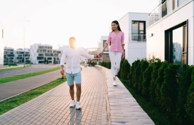 Hafta sonu şehir caddesinde buluşurken taş kaldırımda yürüyen ve erkek arkadaşıyla el ele tutuşan günlük kıyafetlerle neşeli bir kız arkadaş.