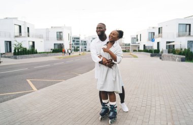 Paten giymiş Afrikalı Amerikalı erkek arkadaş ve kız arkadaşı sevmek. Başka tarafa bakmak, kucaklaşmak ve asfalt şehir caddesinde paten kaymak.