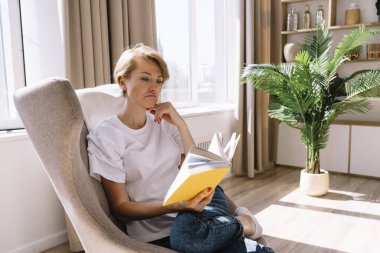 Rahat olmayan bayan, rahat bir odada boş zamanlarında koltukta oturmuş kitap okurken yüzünü buruşturuyor.