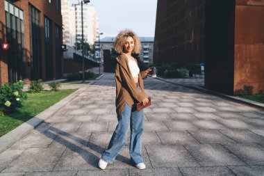 Genç Afro-Amerikan kadınlarının vücudu günlük kıyafetlerle ve sıcak içeceklerle gülümseyerek şehirde yürüyüş yolunda dikilirken kameraya bakıyorlar.