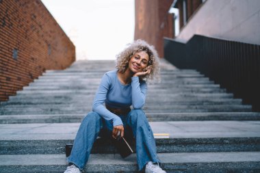 Haftasonu şehir caddesindeki planlayıcıyla merdivenlerde oturan şık kıyafetli, kaygısız siyahi kadın.