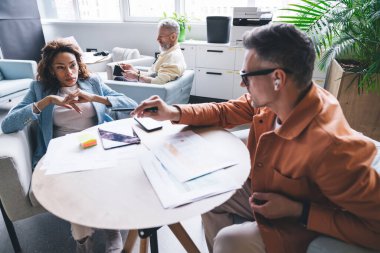 Modern iş merkezinde oturma odasında birlikte otururken ve yeni bir proje üzerinde çalışırken,... günlük giysiler giymiş, cihazlar ve gazete okuyan çok ırklı iş adamlarından.