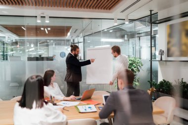 Resmi kıyafet giymiş bir grup meslektaşın, modern toplantı odasında çalışma projesini anlatırken, aynı anda çalışma odasındaki çalışma odasının...