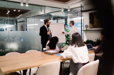 İş arkadaşları beyaz tahtaya yazı yazıp proje detaylarını anlatırken, iş arkadaşları da dizüstü bilgisayarları ve tabletleriyle masada oturup modern yönetim kurulunda ring üzerinden sunum dinliyorlar.