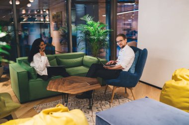 Koltuğunda oturup dizüstü bilgisayarı karıştıran hoş bir çalışan. Bu arada, etnik bayan meslektaşım modern ofiste telefon görüşmesi yapıyor.