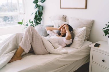 Sağlıksız genç bayan sabahları baş ağrısı çekerken ve kendini iyi hissetmezken evde yatağında uyku tulumu giyerek yatıyor.