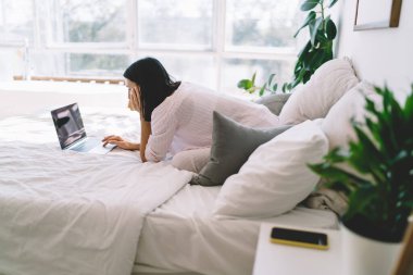 Pijamalı, netbook kullanan ve hafta sonları yatakta dinlenirken kameraya bakan sakin bir kadın.