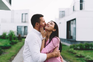 Çok ırklı, genç ve romantik bir çift yolda dikilirken erkek arkadaş iki eli kapalı ve yanaktan öpüyor.