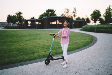 Normal kıyafetler ve spor ayakkabılar giyen, yeşil çimenli çimenlerin yanında tek başına duran, spor ayakkabılı, pozitif bir genç kadın vücudu.