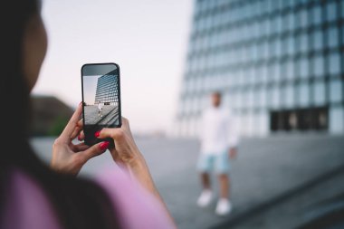 Manikürlü isimsiz bir kadın elinde akıllı bir telefon ve akşam saatlerinde şehrin çok katlı cam binasının yakınında bir adamın fotoğrafını çekiyor.