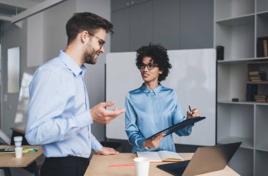 İş adamı, kadın meslektaşının elindeki panoya bakarken, kadın da arkadaşına bakıyor. İş birliği ve takım çalışması. Kafkasyalı bin yıllık meslektaşlar masadalar. Modern başarılı insanlar