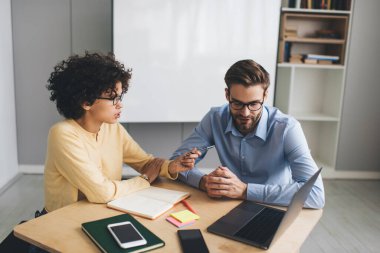 İş kadını, dizüstü bilgisayarından izleyen erkek arkadaşıyla konuşuyor. İş birliği ve takım çalışması kavramı. Genç Kafkasyalı milenyum insanları ofiste masa başında. Modern başarılı insanların fikirleri.