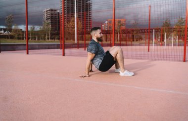 Spor giyim ve spor ayakkabı giyen genç bir erkek sporcunun spor sahasında spor yapmadan önce vücut esneme hareketleri yaparken görüntüsü.