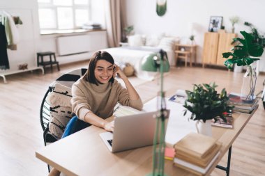 Neşeli, zeki bayan öğrenci netbook 'u karıştırıyor ve açık uzay dairesinde masaya yaslanıp araştırma yapıyor.