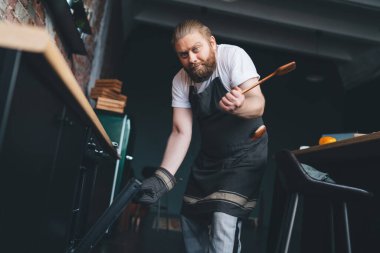 Evdeki mutfakta fırını açarken kameraya bakıp omuz silken önlüklü, kafası karışık ve cüsseli adamın düşük açısı.