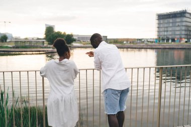 Modern Afro-Amerikalı kadın ve erkeğin deniz kenarındaki çitlerde dikilip şehrin sakin sularına baktıkları arka plan.