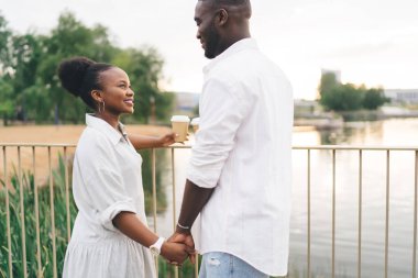 Beyaz gömlekli siyahi adam, Afrika kökenli Amerikalı kız arkadaşıyla kahve içerken el ele tutuşup, deniz kenarında birbirimize bakarken.