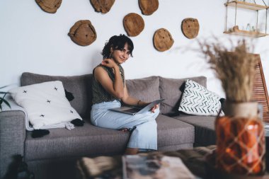 Genç ve çekici bir kadın dizlerinin üzerinde dizlerinin üstüne çöküp Webinar 'la çalışırken oturuyor. Uzaktan çalışan ve evde netbook ile online alışveriş yapan mutlu kadın serbest yazar ağı