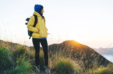 Gün doğumunda Bali 'de yürüyüş yaparken dağlara ve göle bakarken sırt çantasıyla gülümseyen ve başka yöne bakan, mutlu, genç bir kadın.