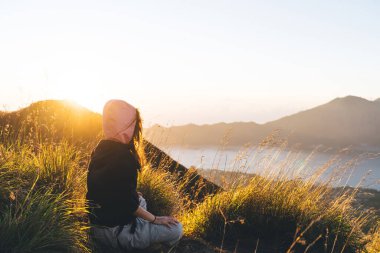 Gün doğumunda Batur Dağı 'nda yürüyüş yaparken Lotus' ta meditasyon yapan, uzun siyah saçlı, isimsiz, barışçıl kadın gezginin yan görüntüsü.