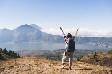 Sırt çantası ve yürüyüş direğiyle, Bali 'deki dağlarda gölün manzarasının keyfini çıkartırken sırt üstü uzanan kaygısız kadın gezginin tüm vücudu.