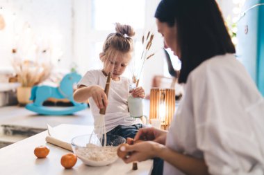 Anne bovlinge yumurta eklerken kız malzemeleri çırpmayla karıştırıyor ve hafta sonunu evde birlikte yemek pişirmenin keyfini çıkarıyor.