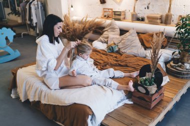 Yatağa oturmuş, pijamalı komik bir kızın saçını yaparken yatak odasında birlikte boş vakit geçirirken pozitifliğin yan görüntüsü.