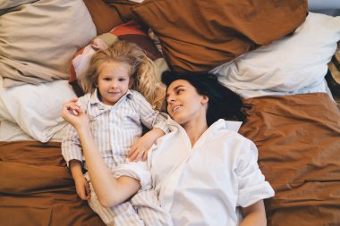 Yukardan gelen sevgi dolu anne ve güzel kızın pijamalarıyla yatakta uzanıp yatak odasında dinlenirken birbirlerini okşaması.