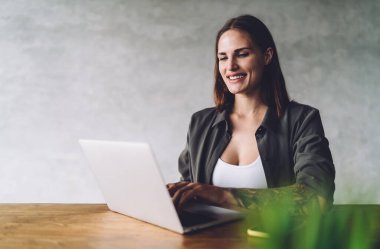 Kolu dövmeli, neşeli, serbest çalışan bir bayan. Masada oturuyor ve gülümsüyor. Kafede dizüstü bilgisayar kullanarak işe başlıyor.