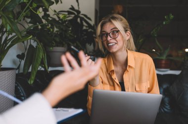 Görsel koruma için gözlük takan Kafkas 'lı mutlu metin yazarı web tasarımı için kırpılmış iş ortaklarıyla iletişimin keyfini çıkarıyor, elinde dizüstü bilgisayar tutan ve gülümseyen neşeli kadın.