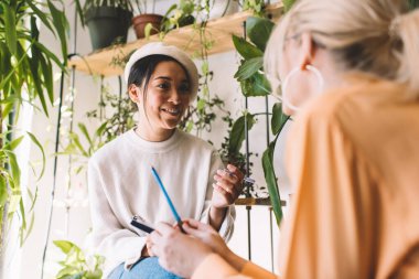 Neşeli Asyalı öğrenci gülerek güler yüzlü gündüz vakti iş arkadaşlarıyla birlikte çalışma alanındaki evrak bilgilerini analiz ederken kapalı alanlarda konuşan neşeli kadın tasarımcılar.