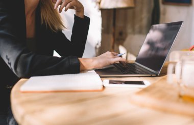 Kafenin iç kısımlarında çalışan tanınmayan bir kadının internet sitesinde internet bilgilerine göz gezdirmesi sırasında gazetecilik yayınını düzenlemek için dizüstü bilgisayar uygulaması kullanan bir kadının yan görünümü