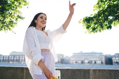 Kolunu kaldırıp parkta kulaklıkla müzik dinlerken gülümseyerek ve yüzünü çevirerek gülümseyen neşeli bir kadın.