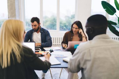 Modern erkek ve kadın çeşitleri yeni bir girişimle iş toplantısı yaparken dizüstü bilgisayarlarla ve kağıtlarla masaya oturuyorlar ve yaratıcı proje hakkında konuşuyorlar.