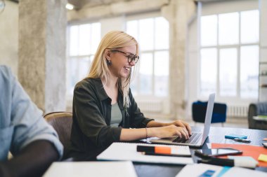 Modern çalışma alanı projesinde çalışırken dizüstü bilgisayarda yazan günlük giysiler ve gözlüklerle genç bayan çalışanın yan görüntüsü