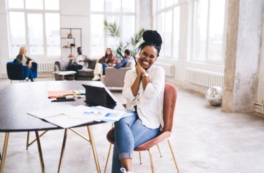Tabletle masada oturan mutlu siyah bayan yaratıcı ofiste kameraya bakarken avuç içlerine katılıyor.