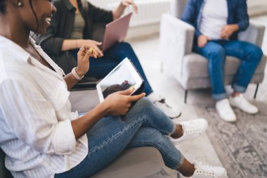 Tanımlanamayan, gündelik giysiler içindeki bir grup insan açık ofis dinlenme odasındaki rahat koltuklarda aletlerle oturuyorlar.