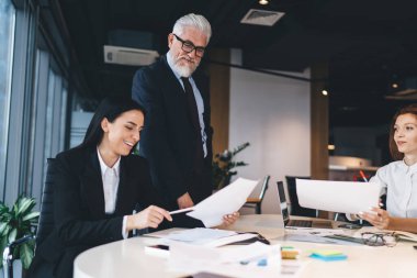 Günümüz iş yerinde yeni projeleri tartışırken erkek patronla resmi kıyafet giyip belgeleri analiz eden bir grup iş arkadaşı.