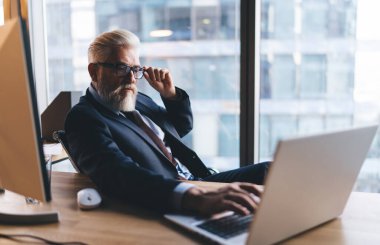 Resmi giyimli ve gözlüklü bir erkek girişimcinin laptopla masaya oturması ve iş yerinde iş projesi üzerinde çalışması