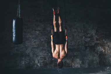 Spor salonundaki jimnastik halkalarında baş aşağı asılı duran güçlü isimsiz erkek sporcunun kas gücünü ve konsantrasyonunu geliştirmeye çalışırken arka plan görüntüsü