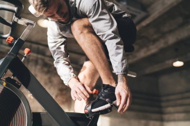Spor kıyafetleri içinde sportif, genç ve güçlü bir erkek sporcunun spor salonunda spor yaparken bisiklet eğitimi için hazırlanması.