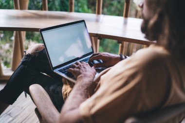 Tahta tezgahta dizüstü bilgisayarla oturan ve uzaktan kumandalı otel odasının balkonunda çalışırken ekrana bakan isimsiz bir serbest erkek.