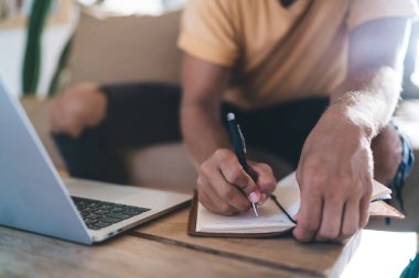 Anonim erkek serbest çalışan, dizüstü bilgisayarla ahşap masada oturuyor ve dizüstü bilgisayar projesinde çalışırken kalemle notlar yazıyor.