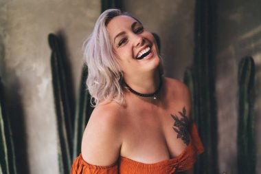 Kafedeki bulanık duvarın yanında durmuş kameraya bakıp gülümseyen boyalı saçlı, neşeli genç bayan turistten.