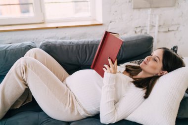 Gebelik hakkında kitap okuyan koca göbekli bir kadın beklerken hafta sonları evdeki kanepede rahat bir şekilde uzanmak...